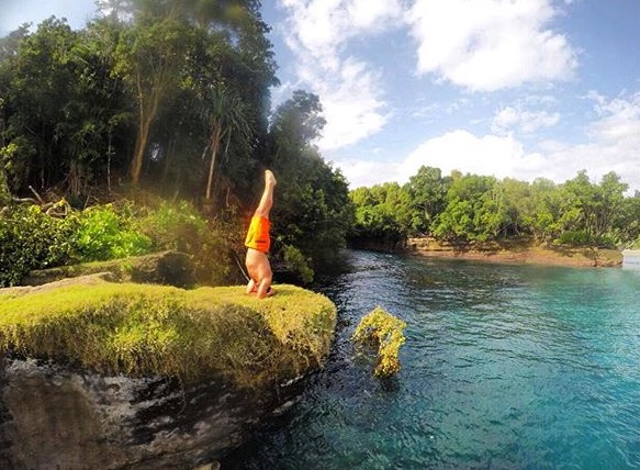 Daniel De Nardi praticando uma invertida sobre as mãos numa pedra à beira de um rio, cercado de natureza